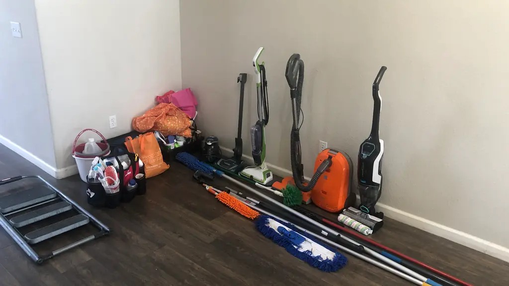 Vacuums, mops, an extension pole and a step stool lined up along the wall of an empty room