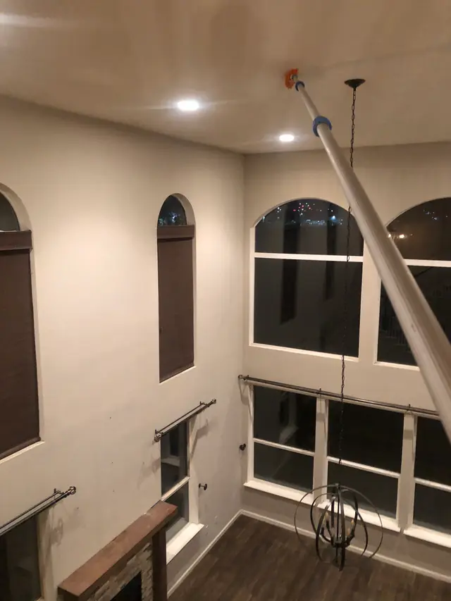 A two-storey living room with arched windows, an extension pole reaching the ceiling